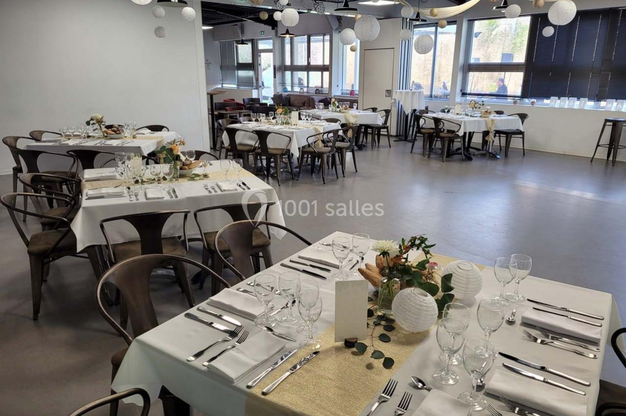 Salle de réception décorée avec des tables dressées, nappes blanches, centres de table floraux et lanternes suspendues.