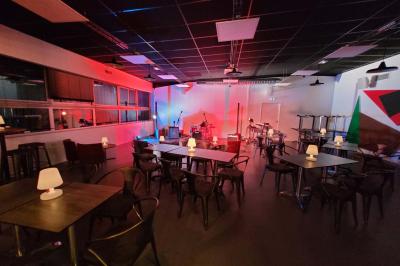 Salle vide avec sol en béton, murs sombres, éclairage au plafond et une table de mixage au fond.