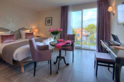 Chambre lumineuse avec un mur rose, deux fauteuils fuchsia, un lit double et des meubles blancs avec miroirs.