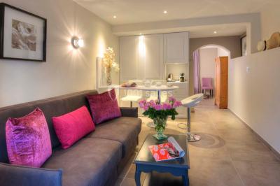 Chambre lumineuse avec un mur rose, deux fauteuils fuchsia, un lit double et des meubles blancs avec miroirs.