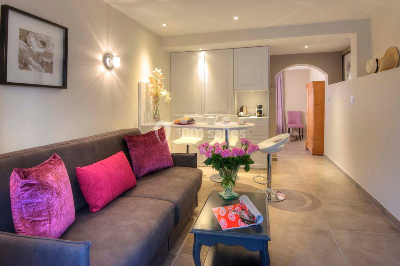 Salon moderne avec canapé gris, coussins roses, table à manger blanche et décoration florale dans un espace lumineux.