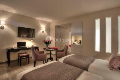 Chambre lumineuse avec un mur rose, deux fauteuils fuchsia, un lit double et des meubles blancs avec miroirs.