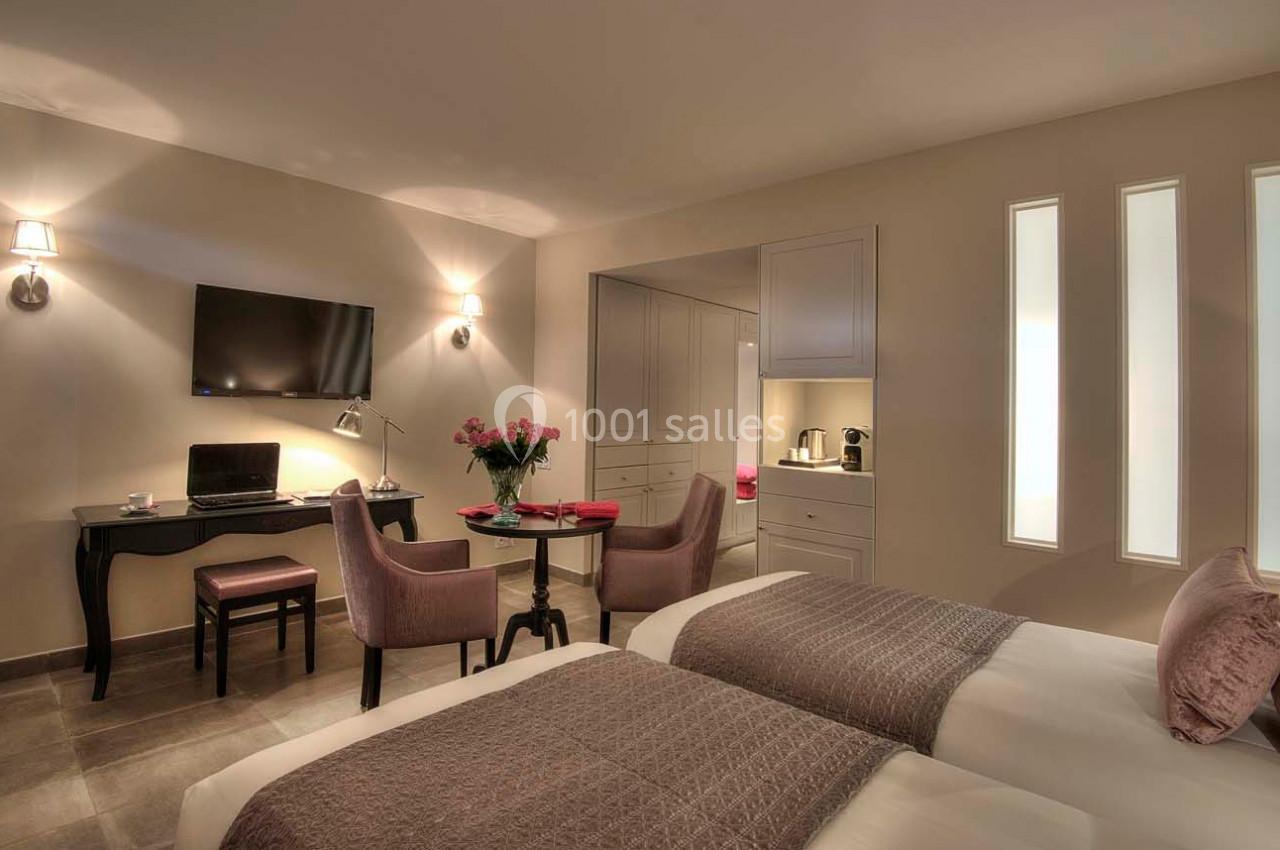 Chambre lumineuse avec deux lits, un bureau, des fauteuils, une table, une télévision et un coin kitchenette.