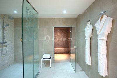 Chambre lumineuse avec un mur rose, deux fauteuils fuchsia, un lit double et des meubles blancs avec miroirs.