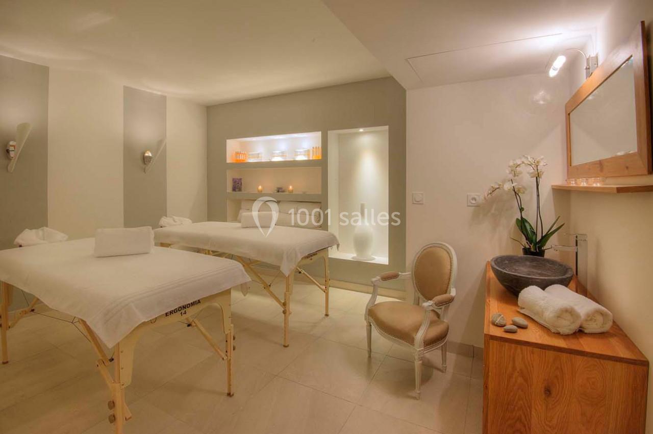 Salle de soins avec deux tables de massage, une chaise, des serviettes pliées et une décoration apaisante.