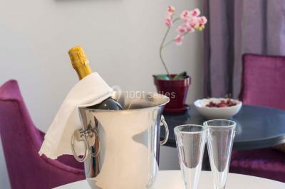 Chambre lumineuse avec un mur rose, deux fauteuils fuchsia, un lit double et des meubles blancs avec miroirs.