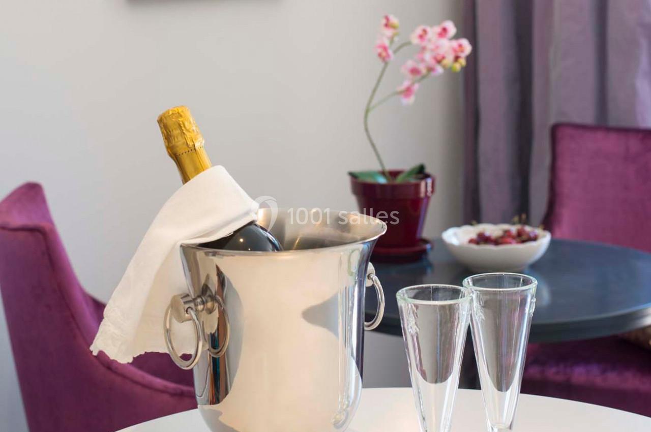 Seau à champagne avec bouteille et serviette sur une table, accompagné de deux flûtes, orchidée et fauteuils en arrière-plan.