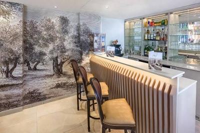 Chambre lumineuse avec un mur rose, deux fauteuils fuchsia, un lit double et des meubles blancs avec miroirs.