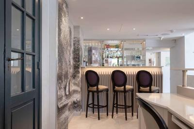 Chambre lumineuse avec un mur rose, deux fauteuils fuchsia, un lit double et des meubles blancs avec miroirs.