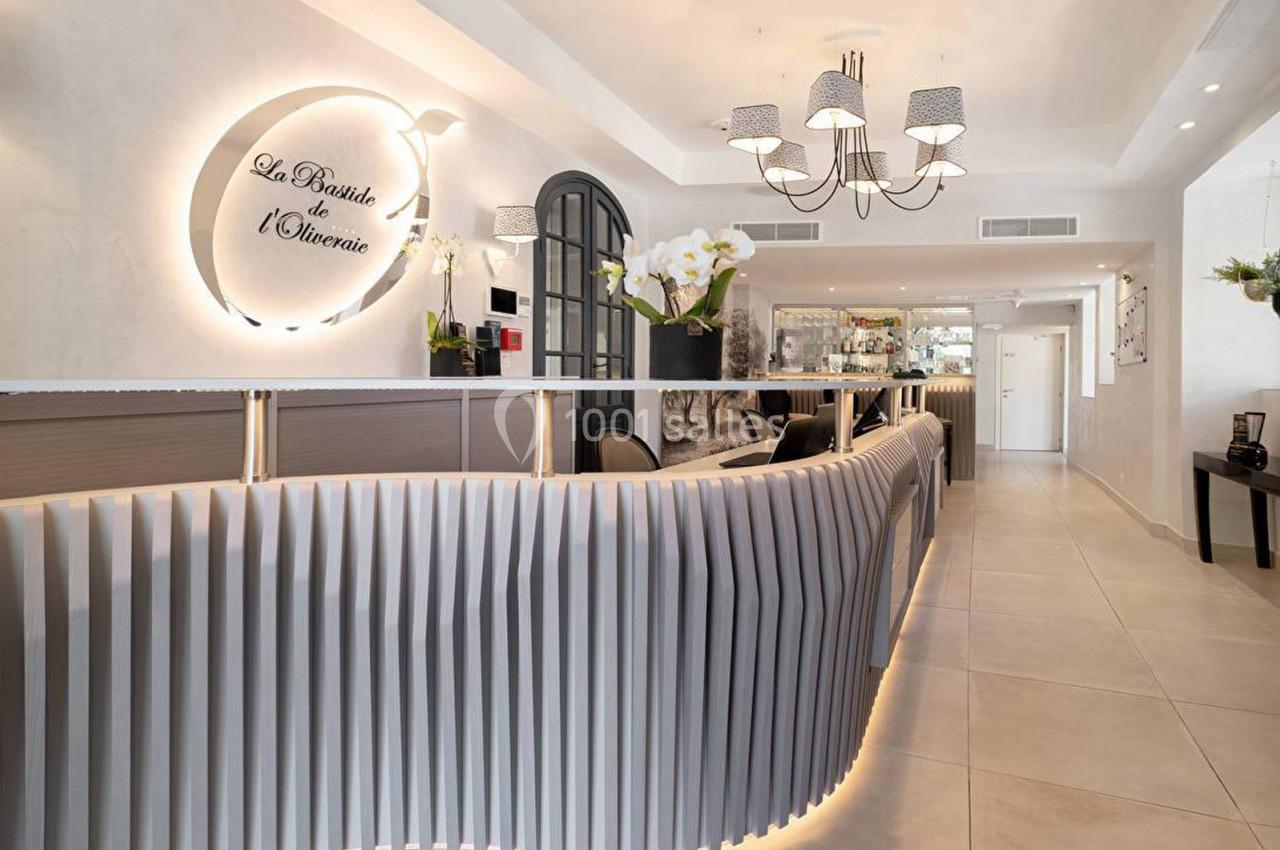 Réception moderne avec comptoir ondulé, éclairage design, orchidées blanches et enseigne murale lumineuse.