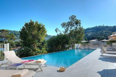 Chambre lumineuse avec un mur rose, deux fauteuils fuchsia, un lit double et des meubles blancs avec miroirs.