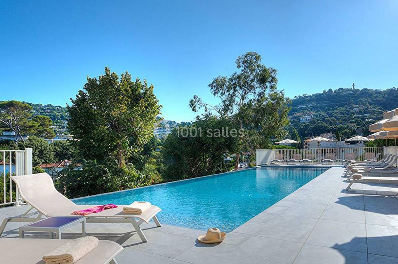 Piscine extérieure avec transats, entourée de verdure et offrant une vue sur des collines sous un ciel dégagé.