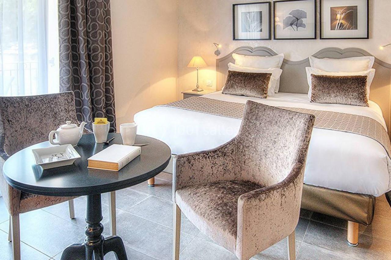 Chambre lumineuse avec lit double, table ronde, deux fauteuils et décor sobre dans des tons neutres.