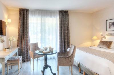 Chambre lumineuse avec un mur rose, deux fauteuils fuchsia, un lit double et des meubles blancs avec miroirs.