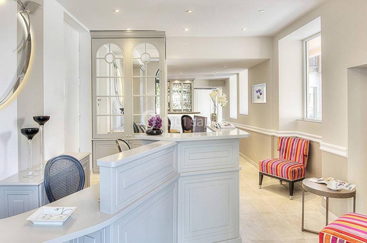 Accueil lumineux avec comptoir blanc, fauteuils colorés, miroir rond éclairé et décoration élégante.