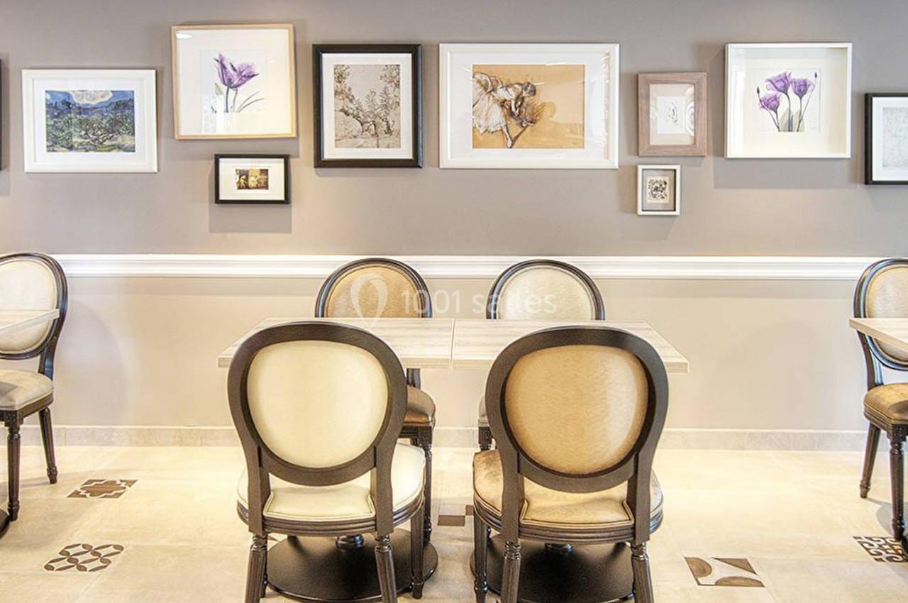Salle lumineuse avec des tables et des chaises élégantes, murs décorés de cadres variés et carrelage clair au sol.