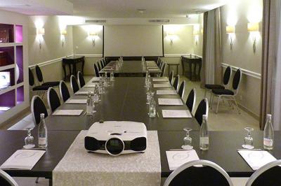 Chambre lumineuse avec un mur rose, deux fauteuils fuchsia, un lit double et des meubles blancs avec miroirs.