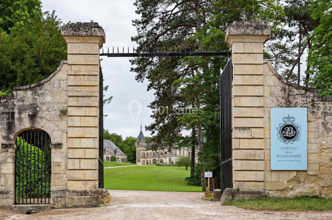 Entrée d'un domaine avec portail en pierre, vue sur un château entouré de pelouses et d'arbres.
