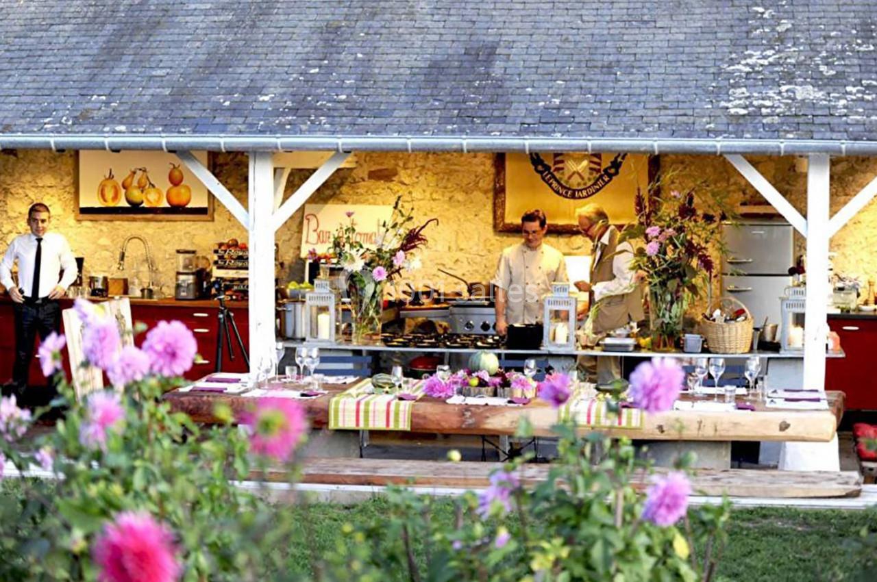 Un stand culinaire en plein air avec des chefs préparant des plats, entouré de fleurs et d'une structure en bois.