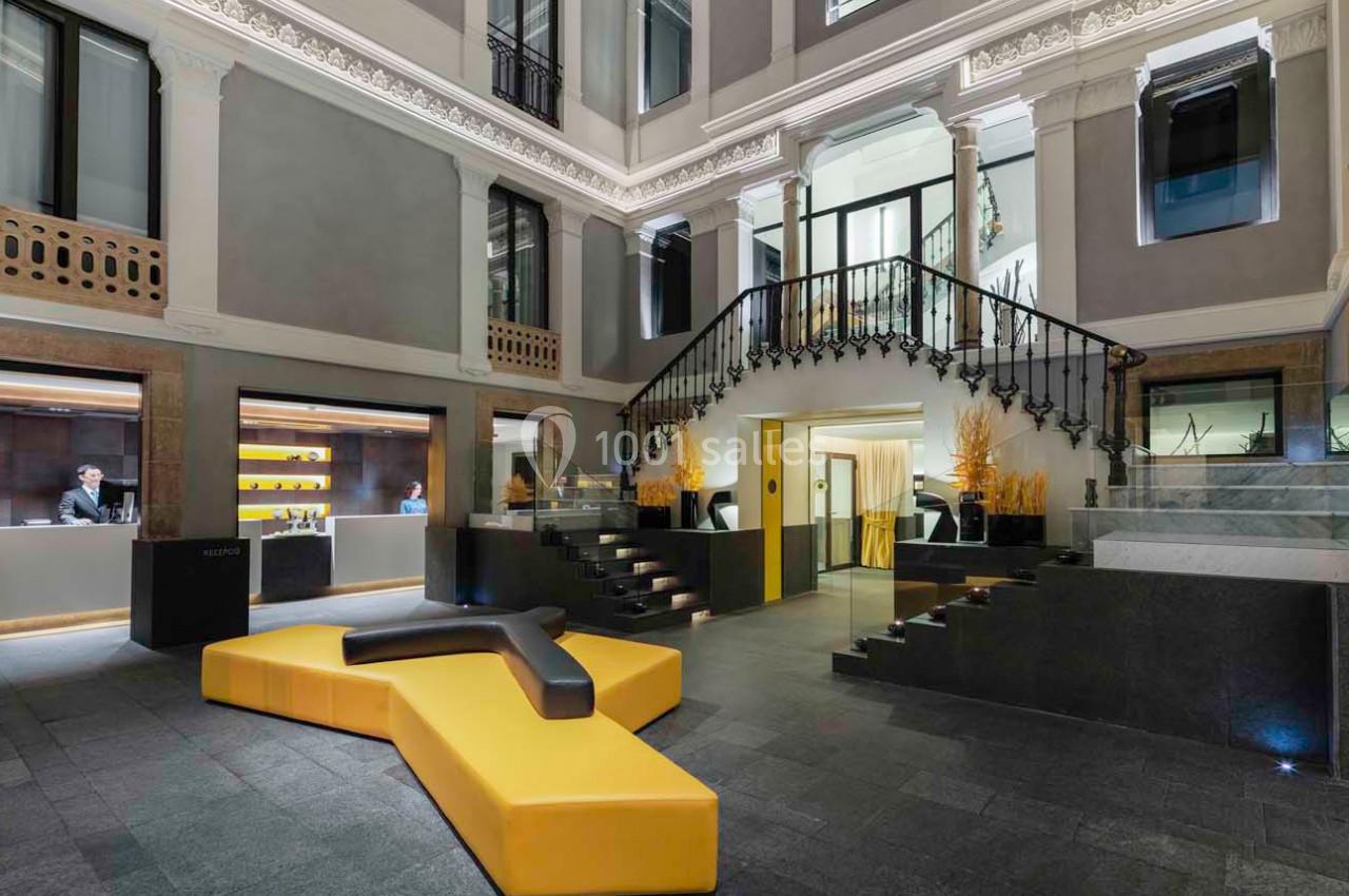 Hall d'entrée moderne avec escalier en fer forgé, comptoir d'accueil et canapé jaune en forme géométrique.