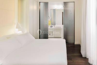 Salle de bain moderne avec douche vitrée, lavabo blanc, miroir rond, fleurs jaunes et mur bleu texturé.