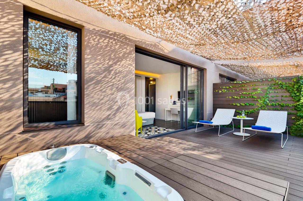 Terrasse avec jacuzzi, chaises longues, table et accès à une chambre, décorée de voiles d'ombrage et plantes grimpantes.