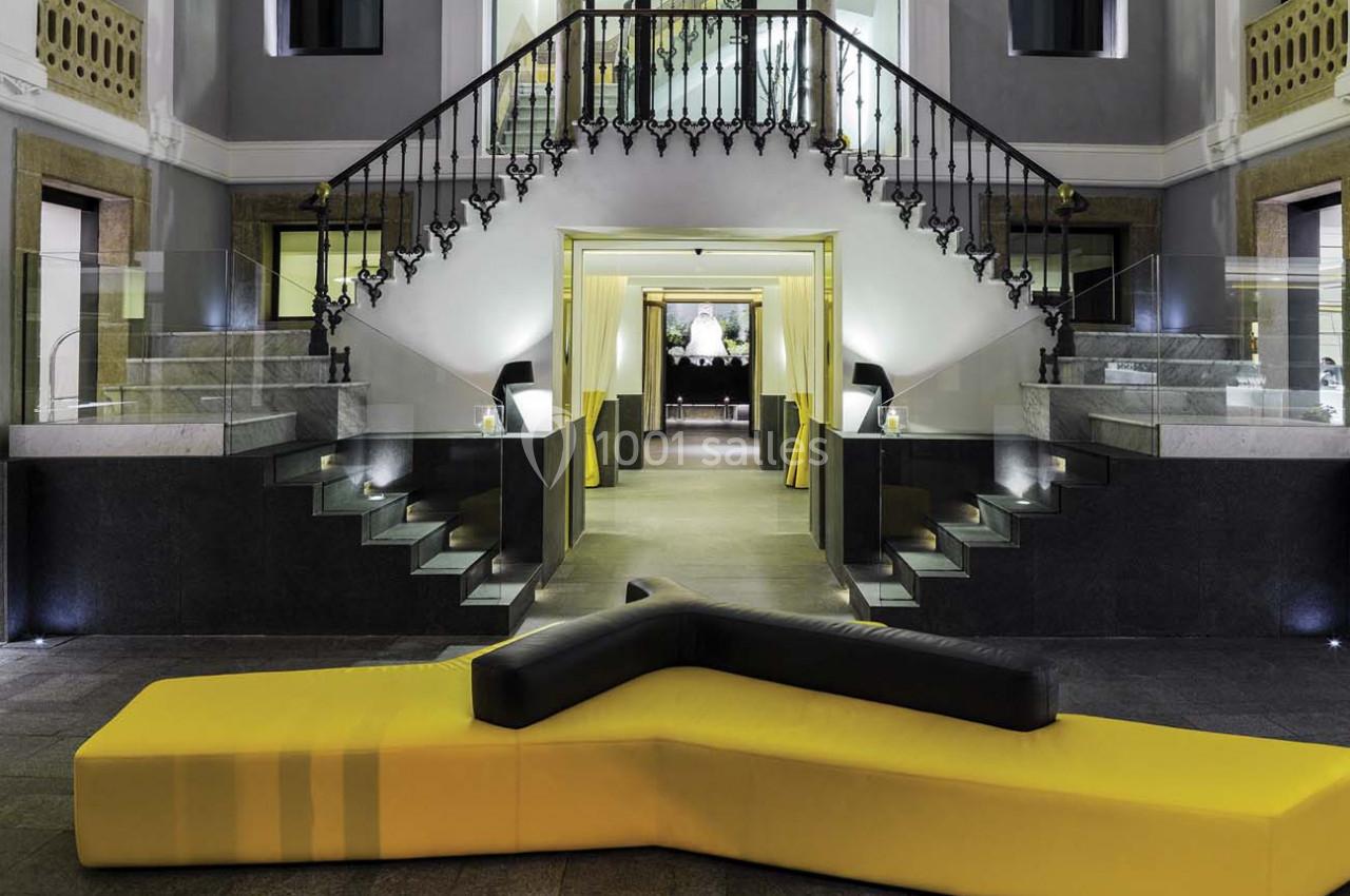 Escalier central élégant avec balustrade en fer forgé, entouré de murs gris et éclairé par des lumières modernes.