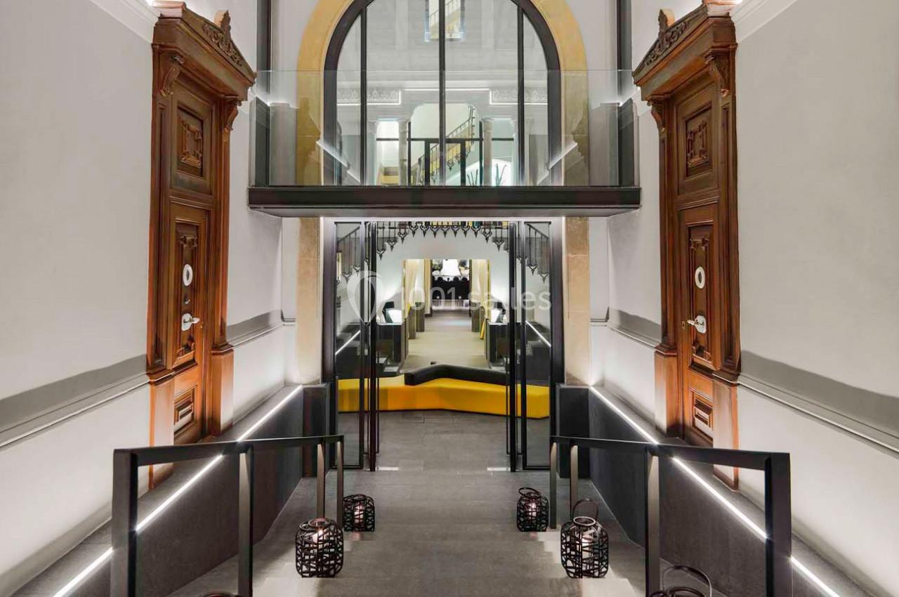 Entrée moderne avec rampes éclairées, portes en bois sculpté et pont en verre menant à un espace intérieur lumineux.