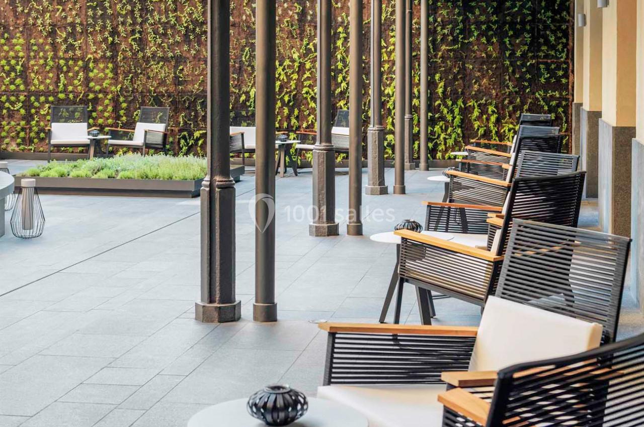 Terrasse avec chaises en bois et métal, tables basses blanches, et mur végétal en arrière-plan.