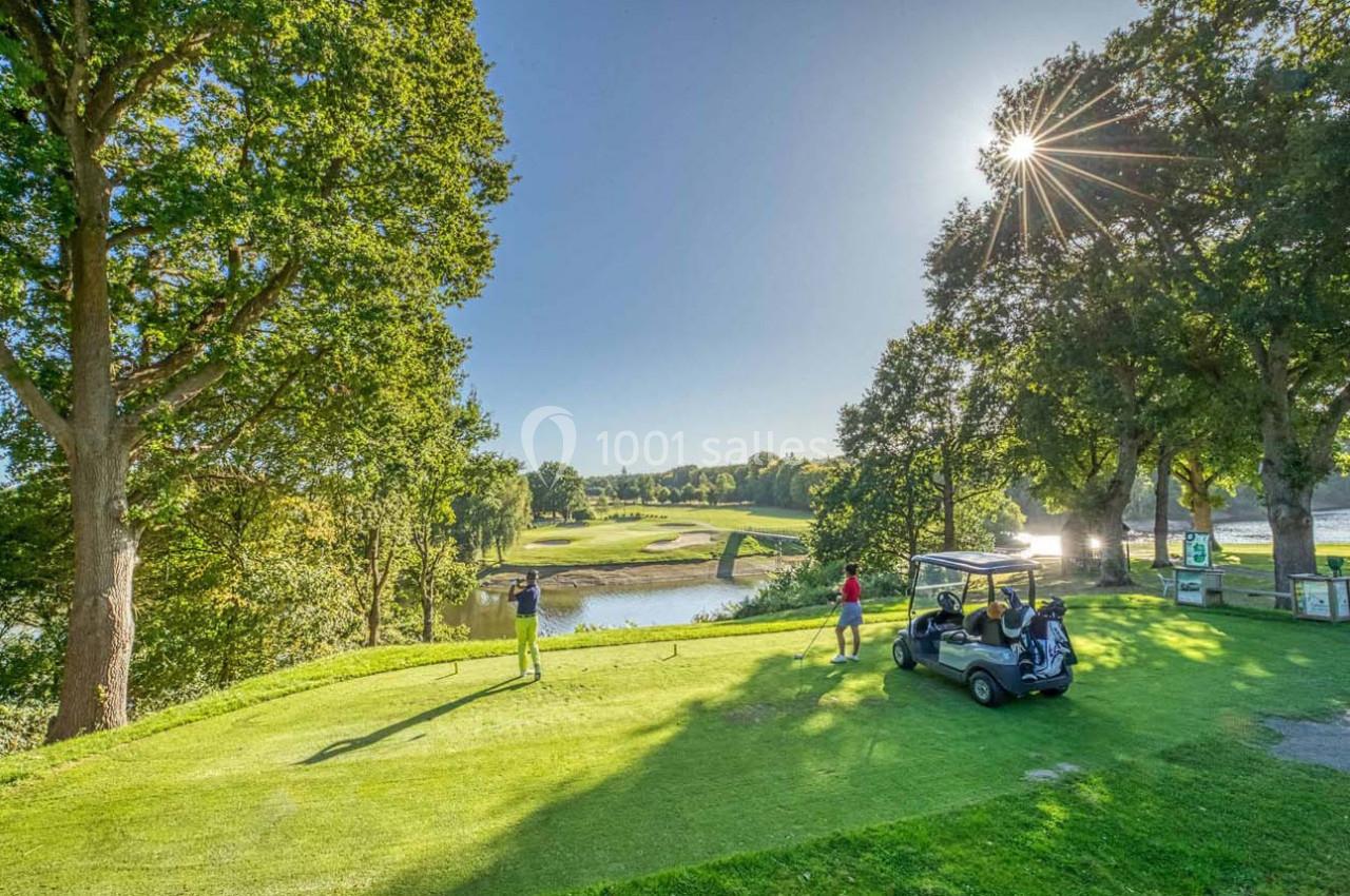 Vue d'un terrain de golf verdoyant avec des arbres, un pont, un étang et des joueurs près d'une voiturette.
