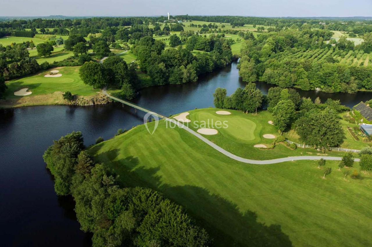 Vue aérienne d'un parcours de golf avec un pont traversant un plan d'eau entouré de verdure et de bunkers.