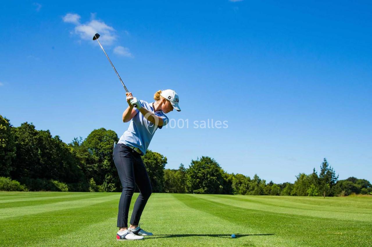 Une golfeuse effectue un swing sur un terrain verdoyant sous un ciel bleu dégagé.