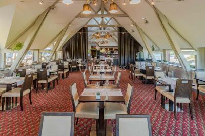 Salle de réunion lumineuse avec poutres apparentes, tables en U dressées avec verres et chaises bleues.