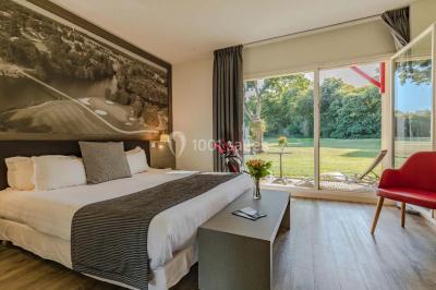 Salle de réunion lumineuse avec poutres apparentes, tables en U dressées avec verres et chaises bleues.