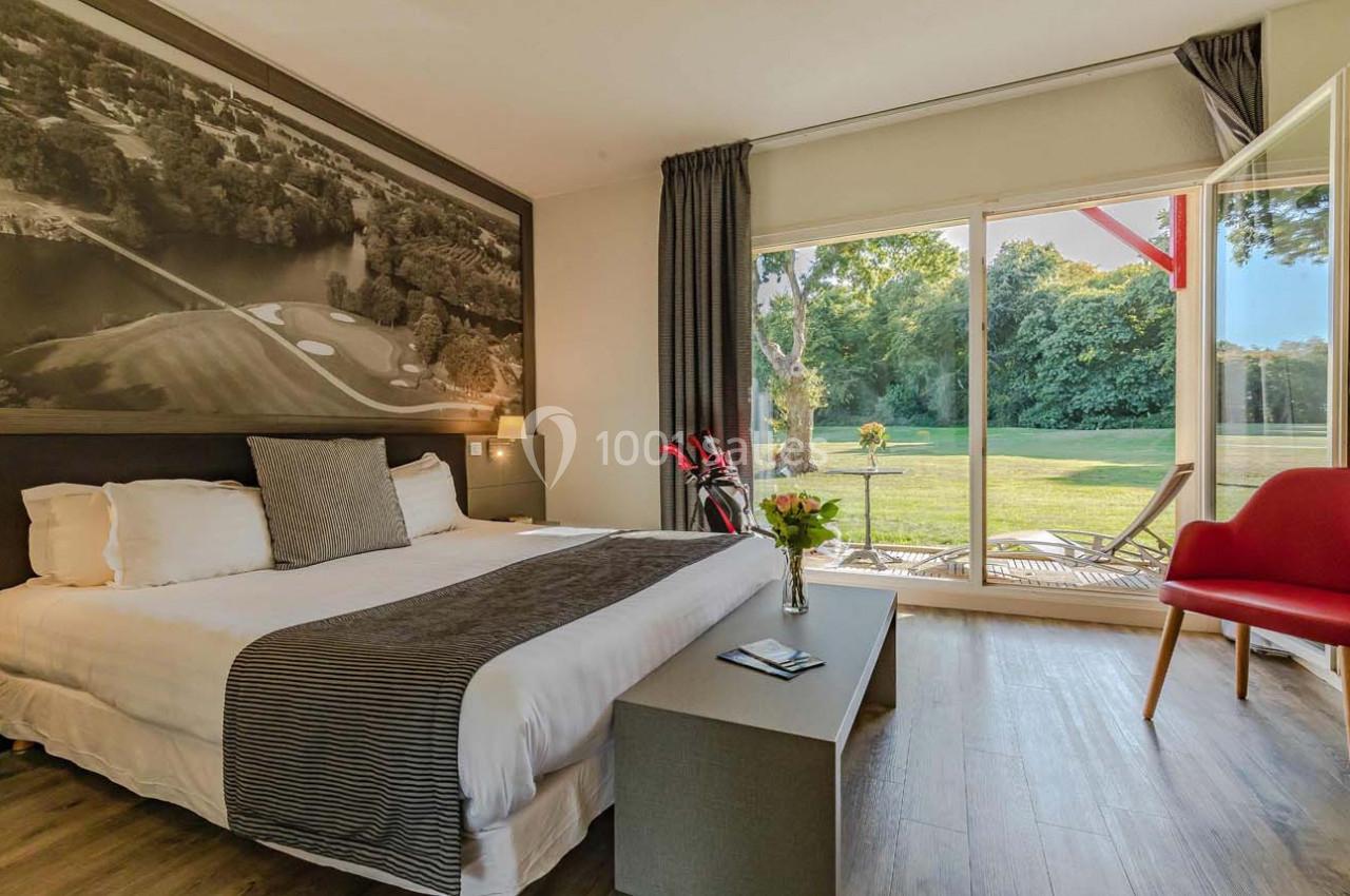 Chambre lumineuse avec lit double, grande baie vitrée donnant sur un jardin verdoyant et terrasse aménagée.