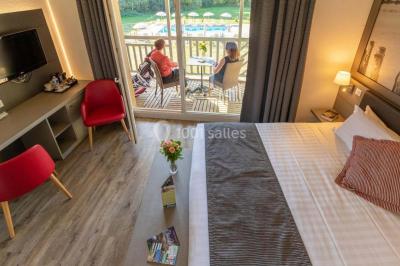 Salle de réunion lumineuse avec poutres apparentes, tables en U dressées avec verres et chaises bleues.