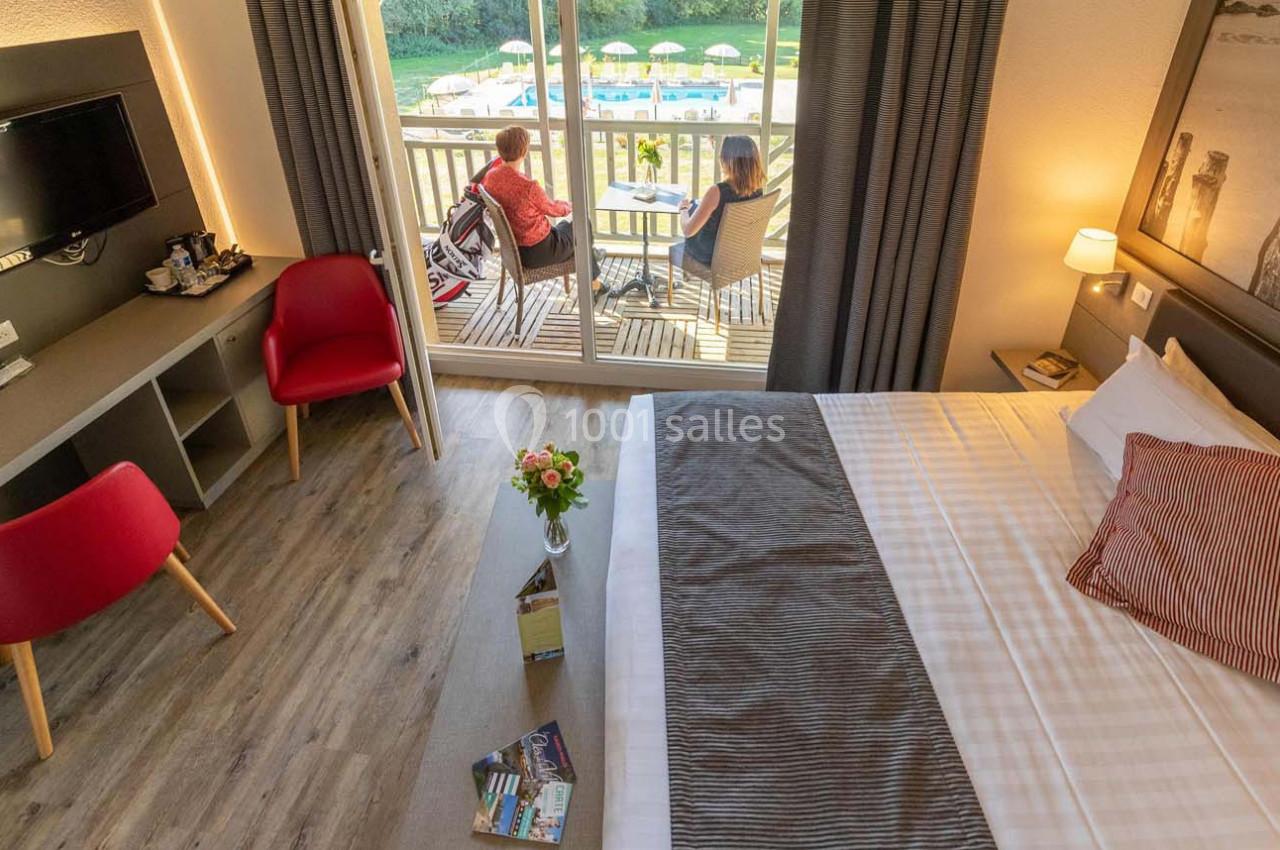 Chambre d'hôtel lumineuse avec lit double, bureau, télévision et balcon donnant sur une piscine extérieure.