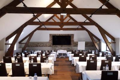Salle de réunion lumineuse avec poutres apparentes, tables en U dressées avec verres et chaises bleues.