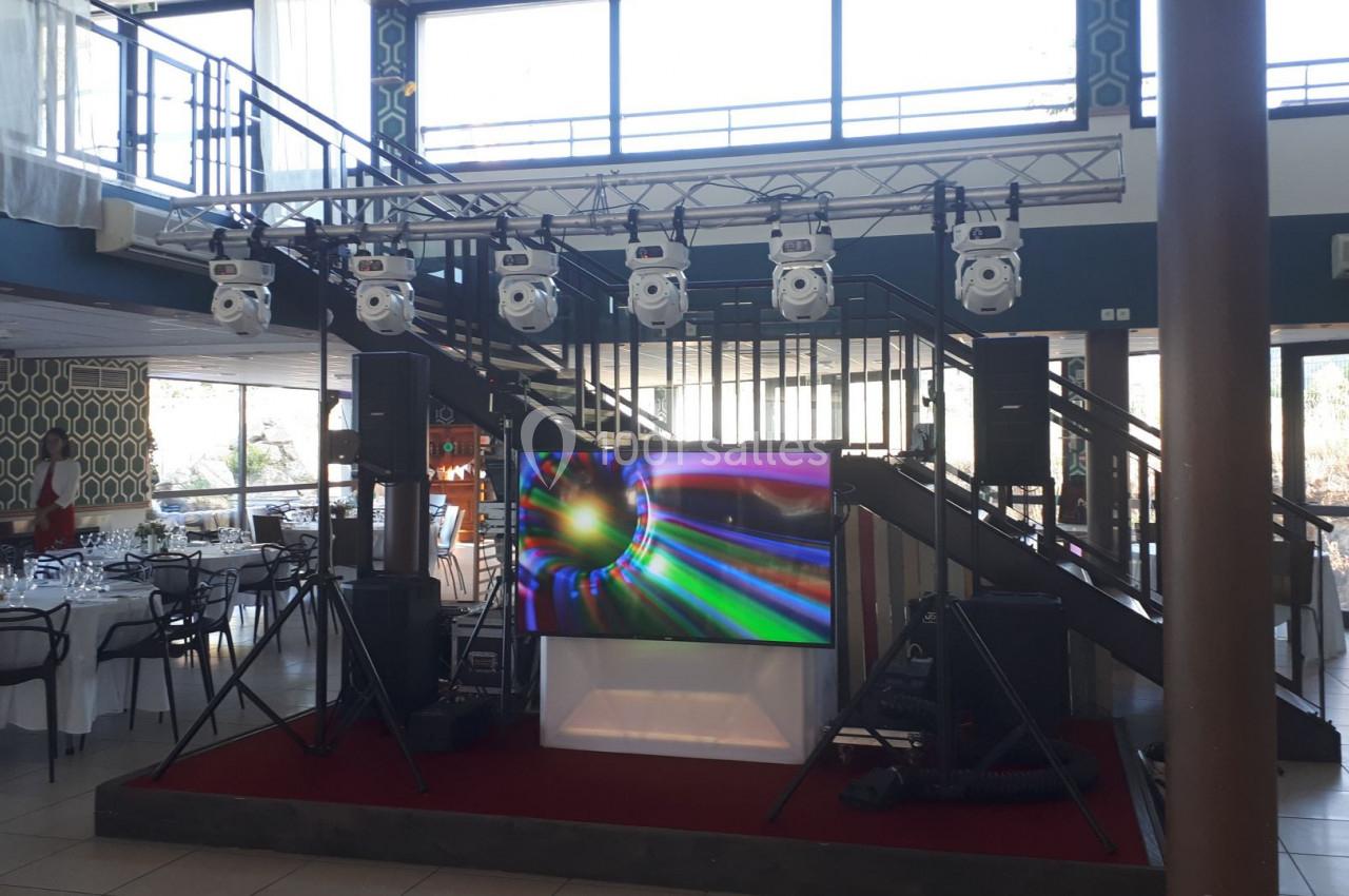 Installation audiovisuelle avec écran lumineux, projecteurs suspendus et haut-parleurs dans une salle de réception.