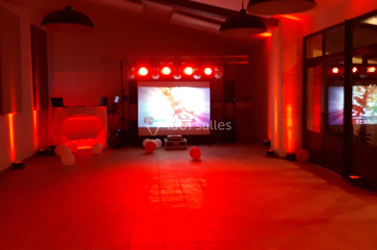 Salle éclairée en rouge avec un écran de projection, des lumières LED et des équipements audio-visuels.