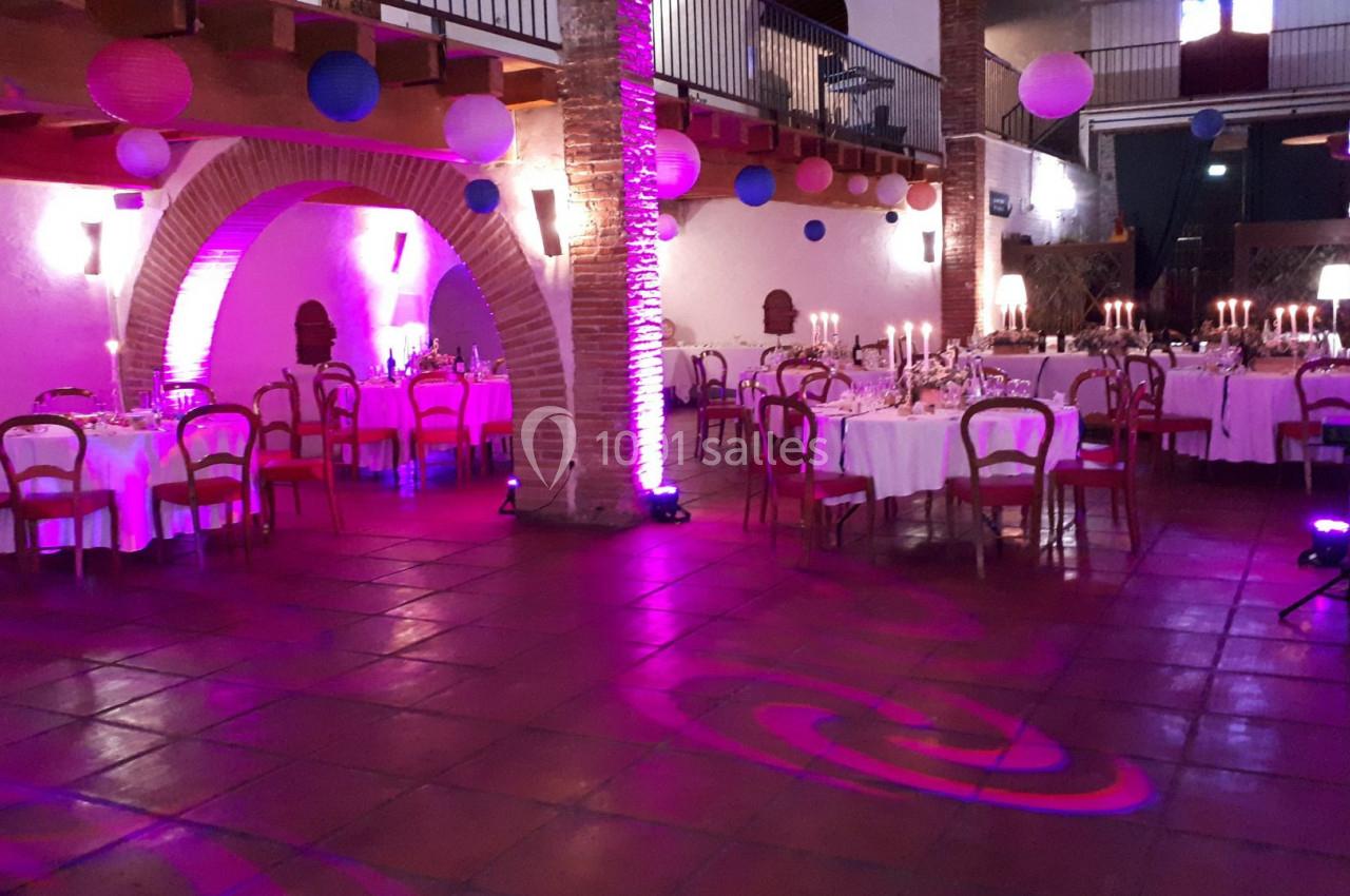 Salle de réception décorée avec des tables rondes dressées, éclairage violet et lanternes suspendues.