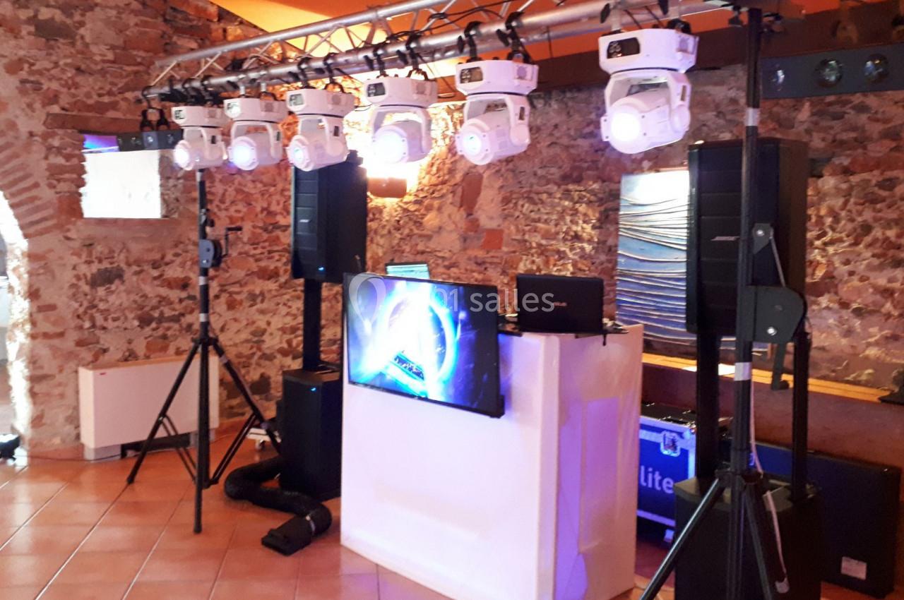 Équipement de son et lumière installé dans une salle en pierre avec un écran et des projecteurs suspendus.