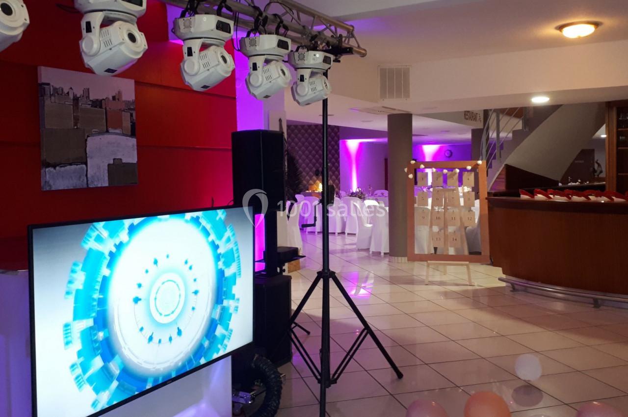 Salle décorée pour un événement avec éclairage coloré, écran, projecteurs et ballons au sol.