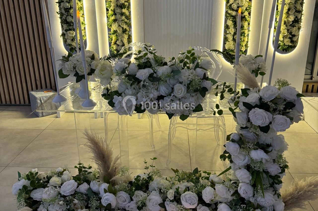 Décor floral élégant avec des roses blanches, des bougies alignées et des panneaux lumineux en arrière-plan.