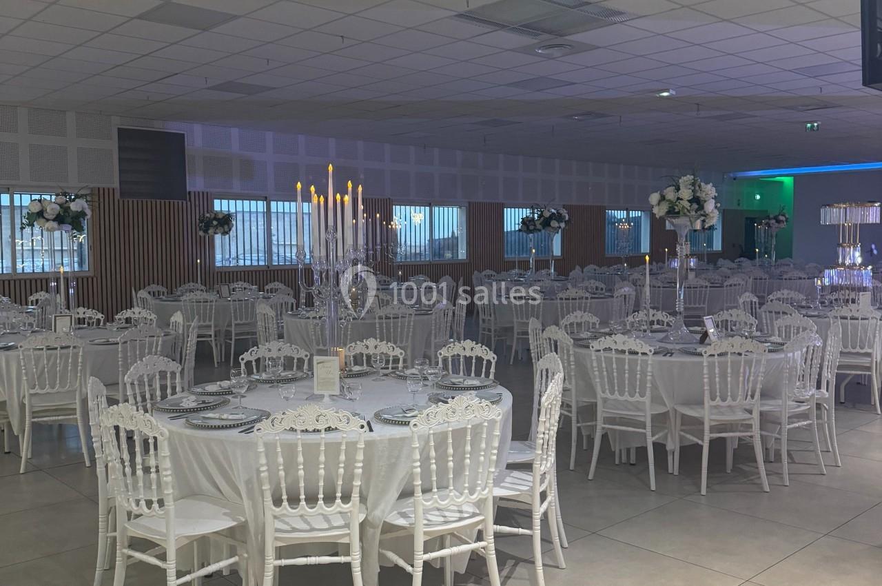 Salle de réception décorée avec des tables rondes dressées, chaises blanches et centres de table élégants.