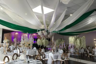 Arc décoratif en fleurs blanches placé dans une salle avec des rideaux gris et un sol en béton.