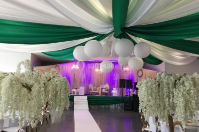 Arc décoratif en fleurs blanches placé dans une salle avec des rideaux gris et un sol en béton.