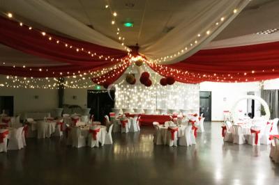 Arc décoratif en fleurs blanches placé dans une salle avec des rideaux gris et un sol en béton.