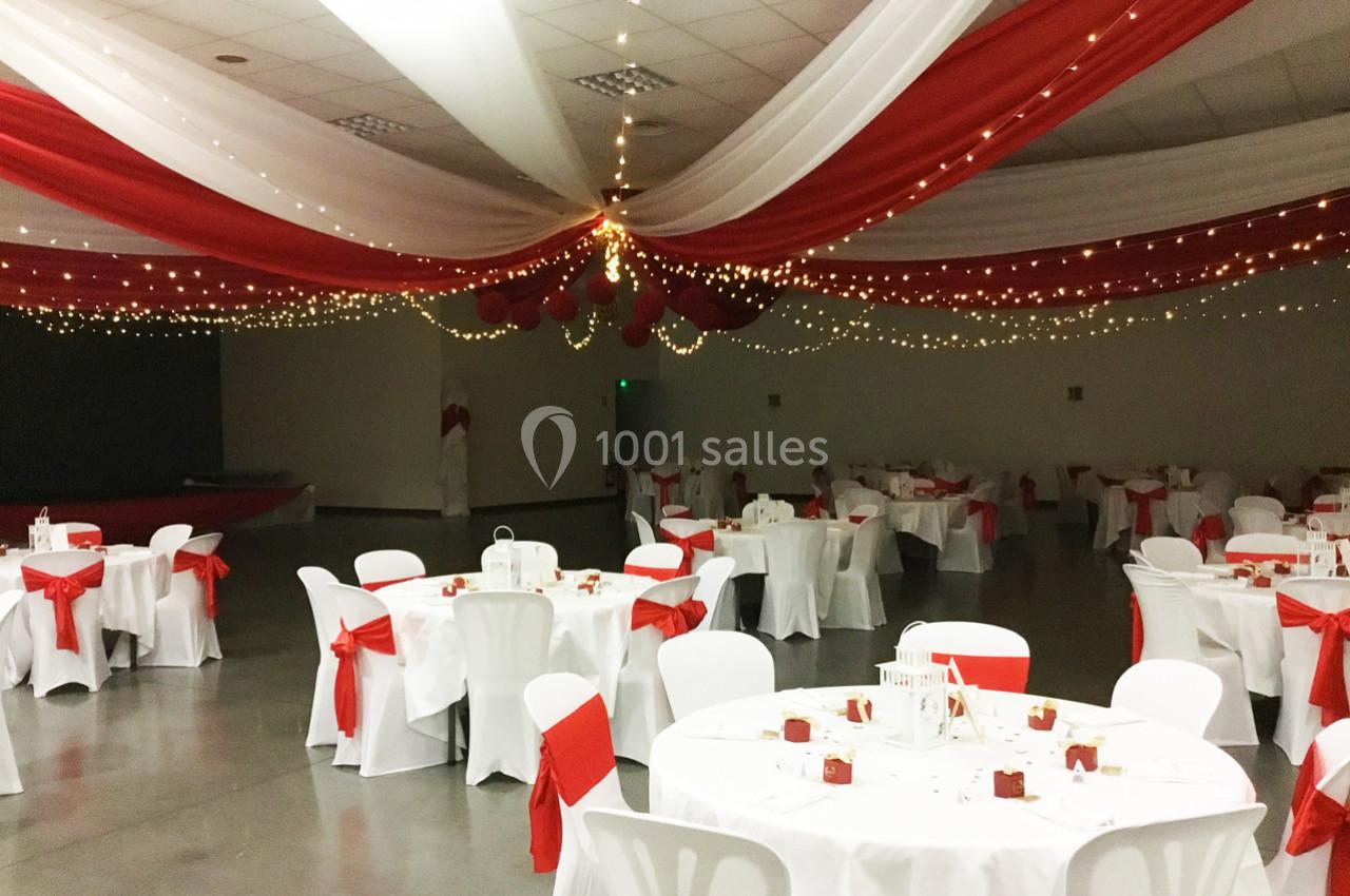 Salle de réception décorée avec des nappes rouges et blanches, des guirlandes lumineuses et des tables dressées.
