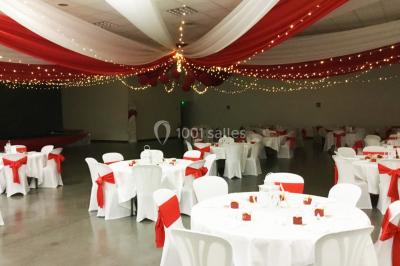 Arc décoratif en fleurs blanches placé dans une salle avec des rideaux gris et un sol en béton.